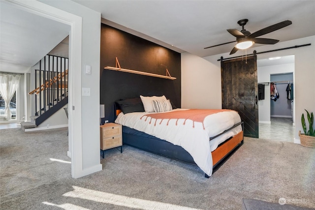 carpeted bedroom with ceiling fan, a walk in closet, and a barn door