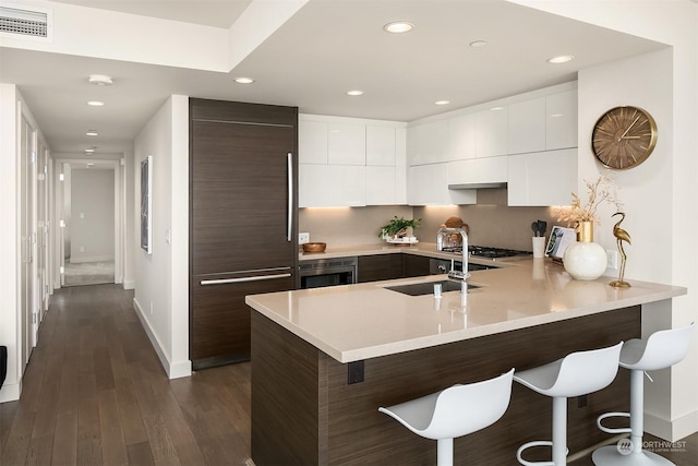 kitchen with white cabinets, sink, dark hardwood / wood-style floors, kitchen peninsula, and a breakfast bar area