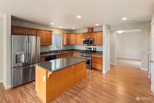 kitchen featuring appliances with stainless steel finishes, a kitchen island, sink, a kitchen breakfast bar, and light wood-type flooring