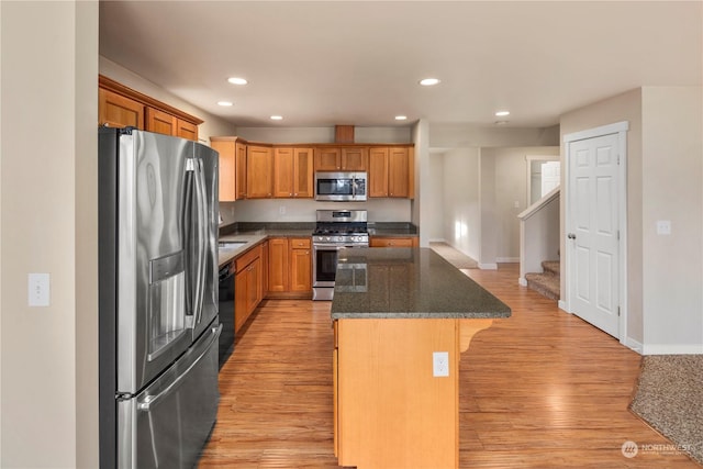 kitchen with appliances with stainless steel finishes, light wood-type flooring, a kitchen bar, dark stone countertops, and a kitchen island