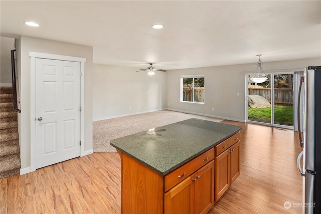 kitchen featuring ceiling fan, decorative light fixtures, a kitchen island, light hardwood / wood-style floors, and stainless steel refrigerator