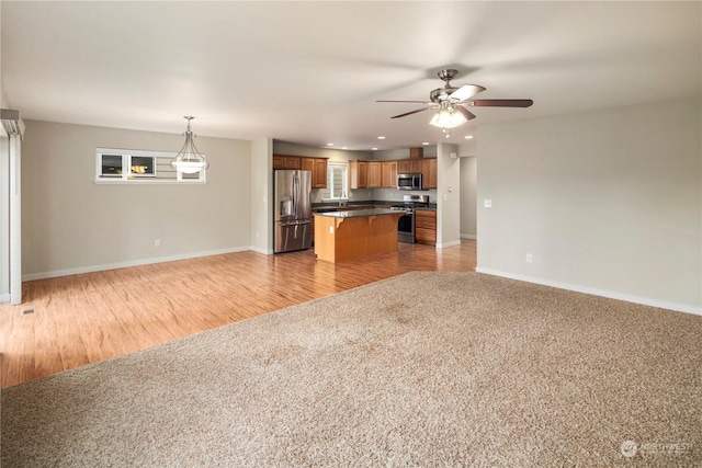 kitchen with ceiling fan, decorative light fixtures, light colored carpet, a center island, and stainless steel appliances