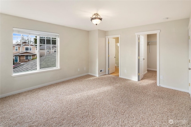 unfurnished bedroom featuring a walk in closet, ensuite bath, light carpet, and a closet