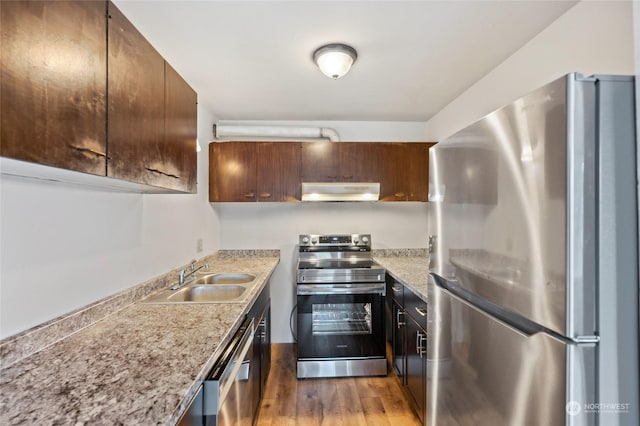 kitchen with stainless steel appliances, light stone countertops, sink, and light hardwood / wood-style floors