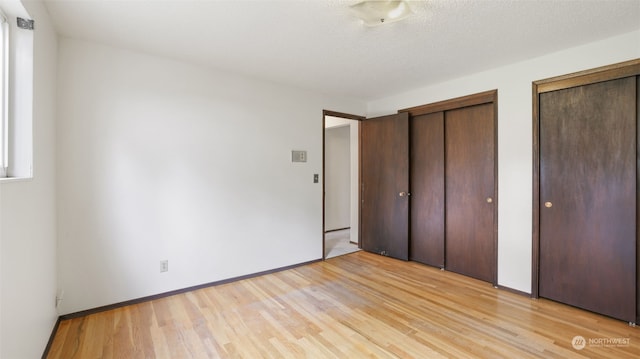 unfurnished bedroom featuring multiple closets, a textured ceiling, and light hardwood / wood-style flooring