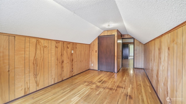 bonus room with a textured ceiling, wood walls, vaulted ceiling, and light hardwood / wood-style flooring