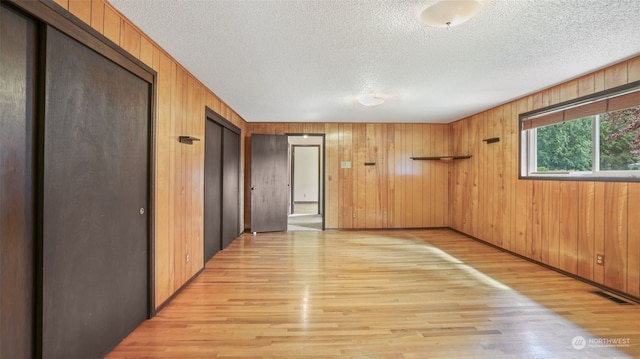 spare room with light wood-type flooring, wooden walls, and a textured ceiling