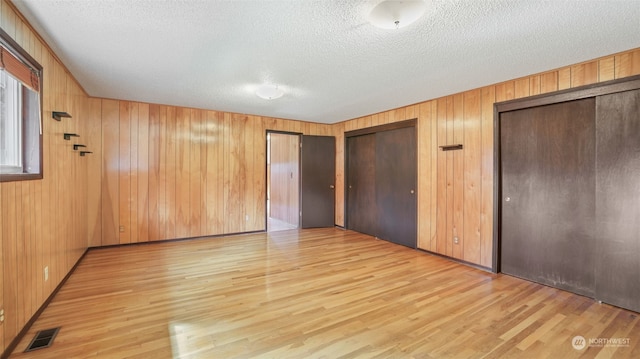 unfurnished bedroom featuring wooden walls, a textured ceiling, light wood-type flooring, and two closets