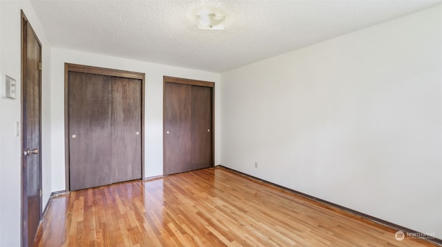 unfurnished bedroom featuring two closets, light hardwood / wood-style flooring, and a textured ceiling