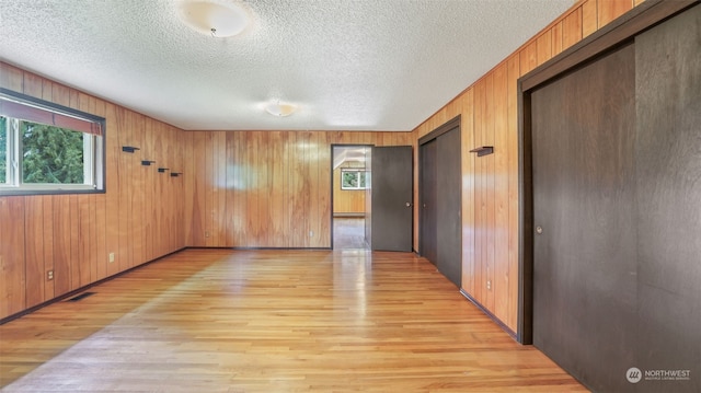 empty room featuring a textured ceiling, wood walls, and light hardwood / wood-style floors