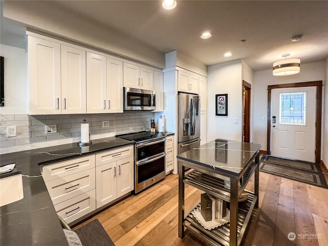 kitchen with light wood-type flooring, backsplash, appliances with stainless steel finishes, and white cabinetry