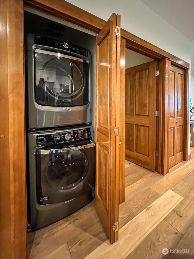 clothes washing area featuring stacked washing maching and dryer and light wood-type flooring