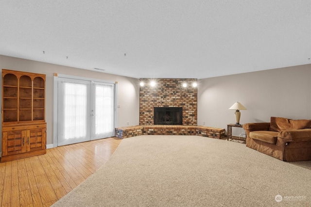 unfurnished living room featuring french doors, light hardwood / wood-style flooring, a textured ceiling, and a brick fireplace