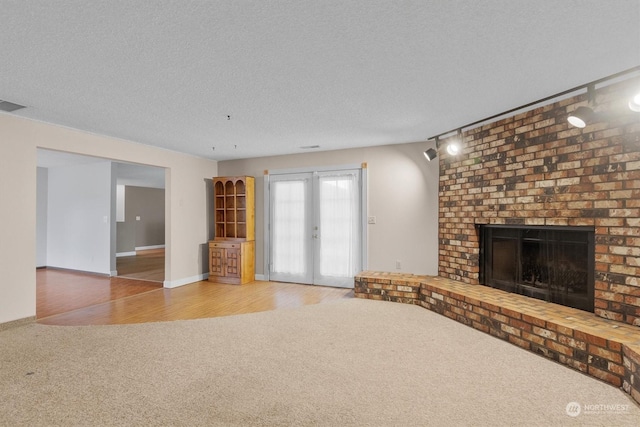 unfurnished living room with carpet flooring, french doors, a textured ceiling, and a fireplace