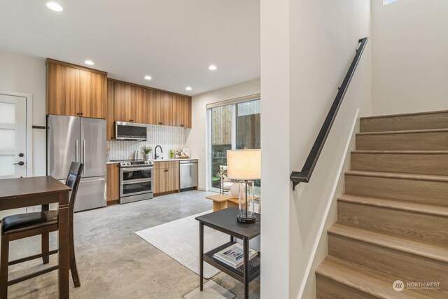 kitchen featuring backsplash, recessed lighting, stainless steel appliances, brown cabinetry, and concrete flooring