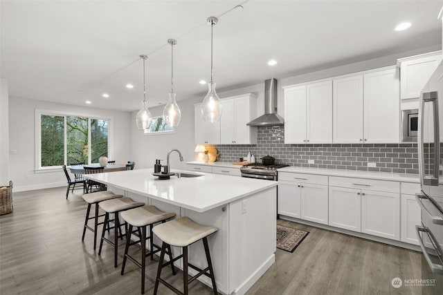 kitchen featuring white cabinets, sink, a kitchen island with sink, and wall chimney range hood