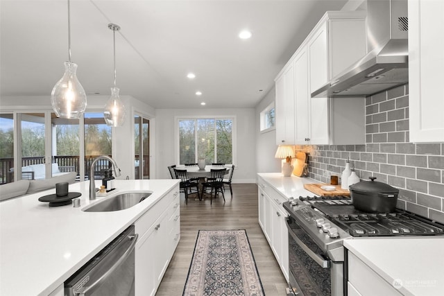 kitchen with appliances with stainless steel finishes, backsplash, wall chimney exhaust hood, sink, and decorative light fixtures