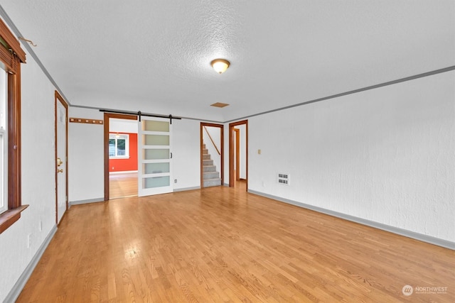 interior space featuring built in shelves, a barn door, light wood-type flooring, and a textured ceiling