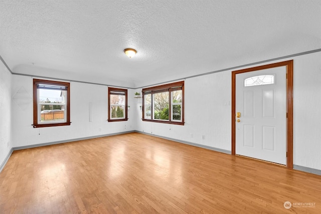 foyer entrance with a textured ceiling, light wood-type flooring, plenty of natural light, and crown molding