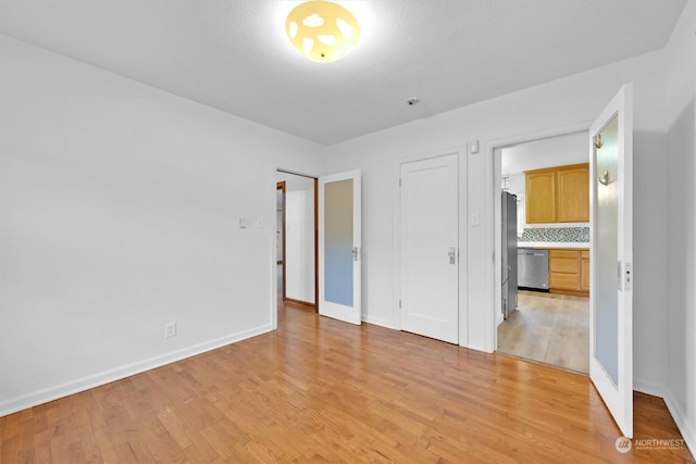 unfurnished bedroom with stainless steel fridge and light hardwood / wood-style flooring