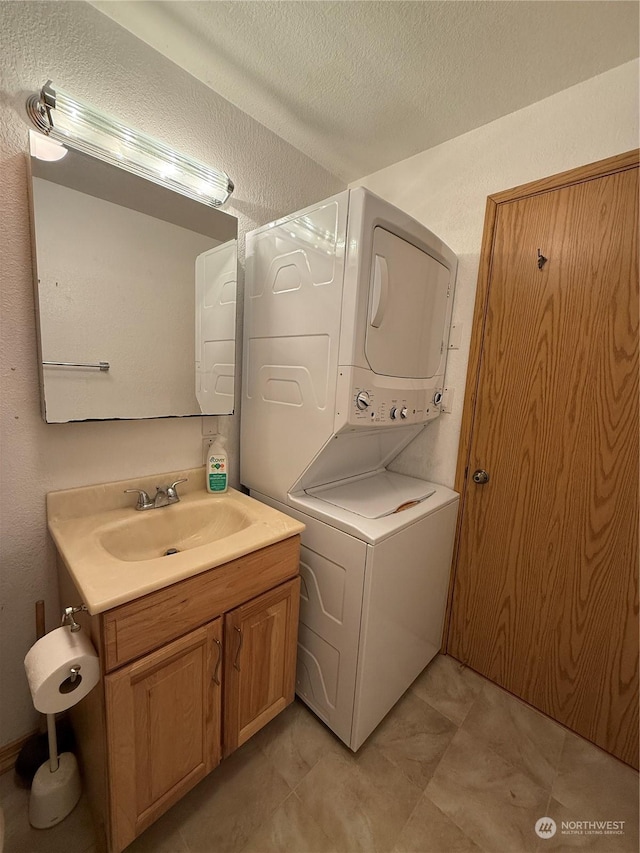 washroom featuring stacked washer / dryer, sink, and a textured ceiling