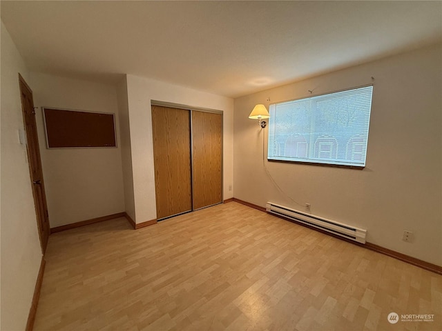 unfurnished bedroom featuring light wood-type flooring, a closet, and baseboard heating