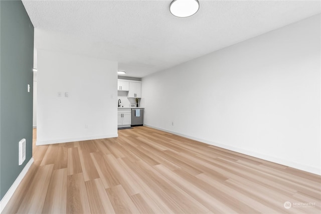 unfurnished living room with a textured ceiling, light wood-type flooring, and sink