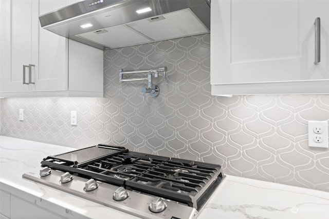 kitchen with light stone countertops, tasteful backsplash, wall chimney exhaust hood, white cabinets, and stainless steel gas stovetop