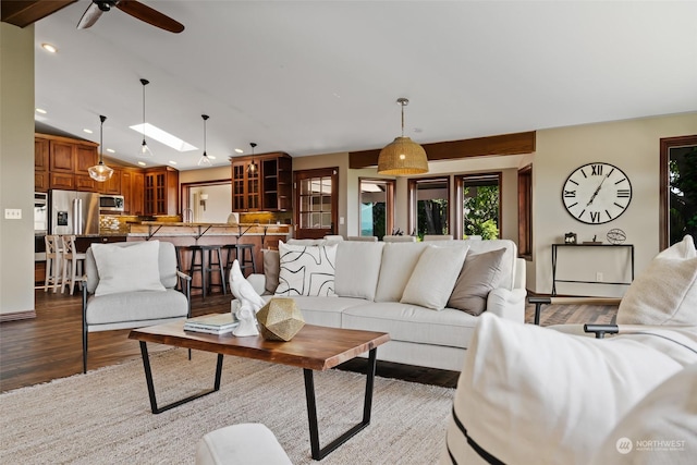 living room with ceiling fan, light wood-type flooring, and lofted ceiling with skylight