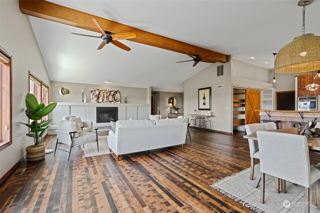 living room with ceiling fan, dark wood-type flooring, a barn door, a fireplace, and vaulted ceiling with beams