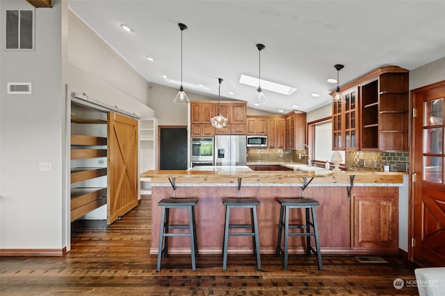 kitchen featuring kitchen peninsula, stainless steel appliances, lofted ceiling with skylight, a barn door, and decorative light fixtures