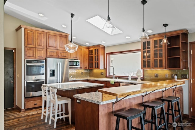 kitchen with a breakfast bar area, lofted ceiling with skylight, stainless steel appliances, and dark hardwood / wood-style floors