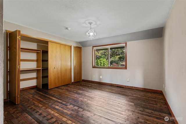 unfurnished bedroom featuring a notable chandelier, dark hardwood / wood-style floors, lofted ceiling, and a closet