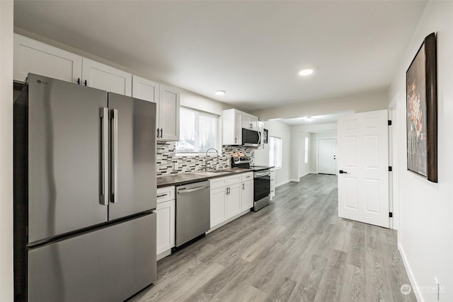 kitchen featuring sink, stainless steel appliances, backsplash, white cabinets, and light wood-type flooring