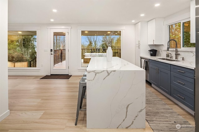 kitchen with a kitchen bar, white cabinets, sink, a kitchen island, and light stone counters