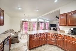 kitchen featuring ceiling fan with notable chandelier, vaulted ceiling, stainless steel dishwasher, and kitchen peninsula