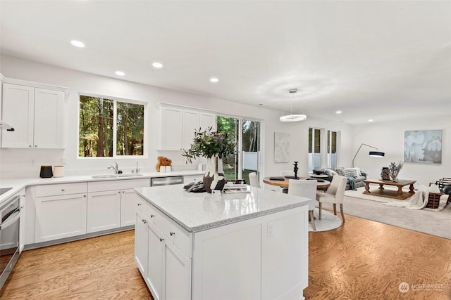 kitchen with sink, white cabinets, hanging light fixtures, and light hardwood / wood-style flooring