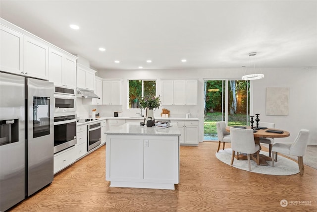 kitchen featuring stainless steel appliances, sink, decorative light fixtures, a center island, and white cabinetry