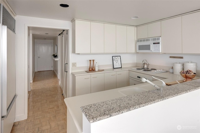 kitchen featuring kitchen peninsula, white appliances, light parquet floors, sink, and white cabinets