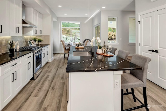 kitchen featuring stainless steel gas stove, tasteful backsplash, a center island with sink, wall chimney exhaust hood, and a sink