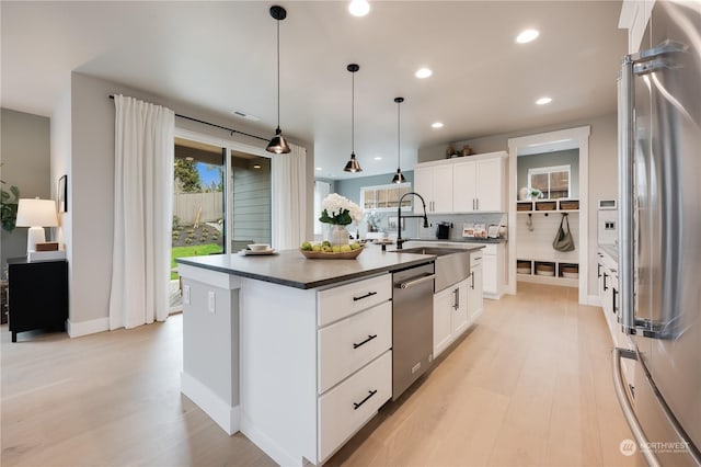 kitchen with stainless steel appliances, sink, white cabinets, hanging light fixtures, and an island with sink