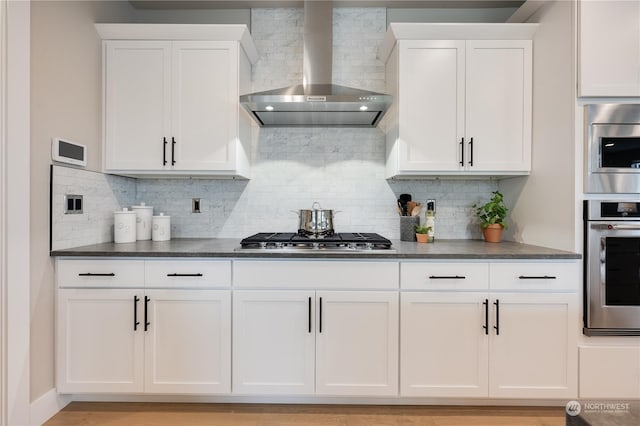 kitchen featuring white cabinetry, wall chimney range hood, stainless steel appliances, and tasteful backsplash