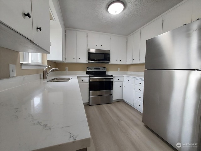 kitchen featuring a textured ceiling, light hardwood / wood-style floors, white cabinets, appliances with stainless steel finishes, and sink