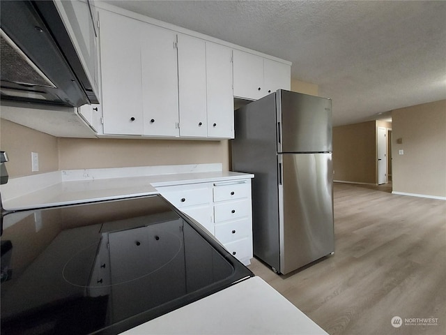 kitchen with white cabinets, a textured ceiling, light wood-type flooring, and stainless steel fridge