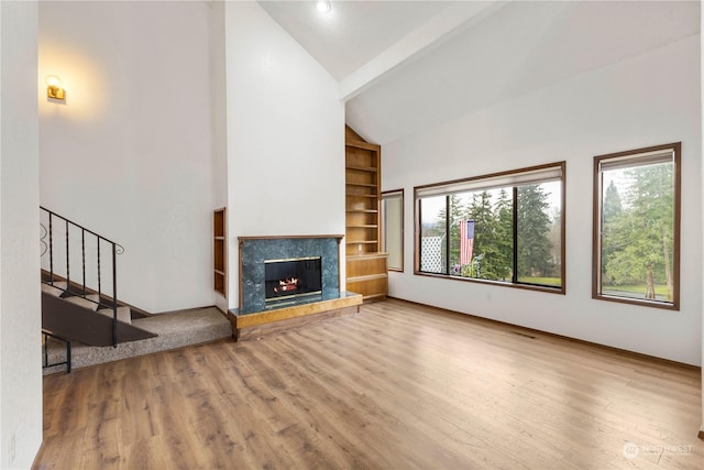 unfurnished living room featuring hardwood / wood-style floors, beam ceiling, plenty of natural light, and a premium fireplace