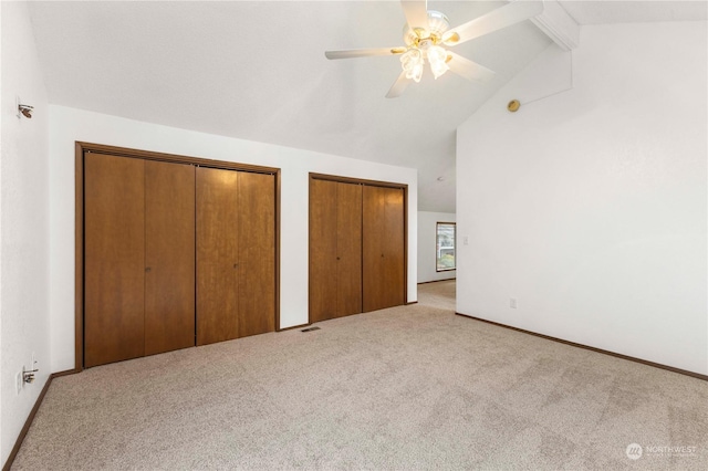 unfurnished bedroom featuring two closets, vaulted ceiling with beams, light colored carpet, and ceiling fan