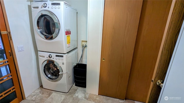 clothes washing area featuring stacked washing maching and dryer and stone finish flooring