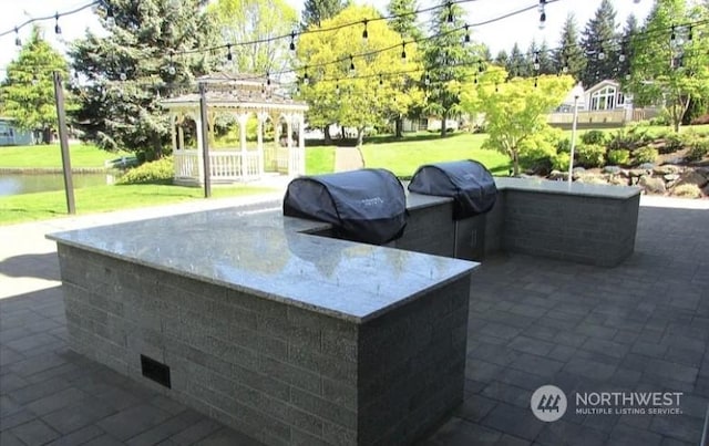 view of patio / terrace featuring a water view, a grill, and exterior kitchen