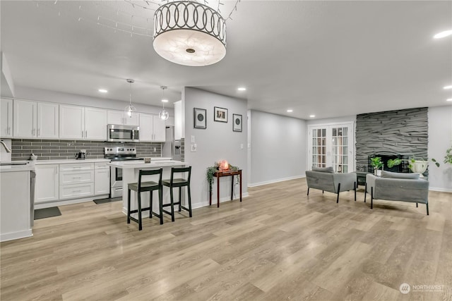 kitchen featuring light wood-type flooring, white cabinetry, stainless steel appliances, and hanging light fixtures