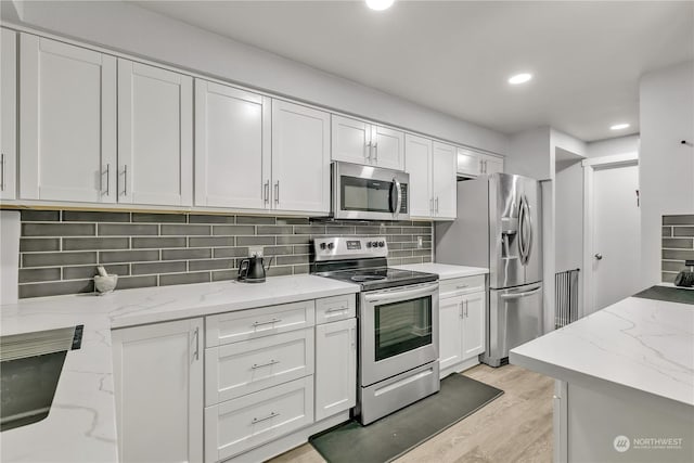 kitchen featuring white cabinetry, light stone counters, light hardwood / wood-style flooring, decorative backsplash, and appliances with stainless steel finishes